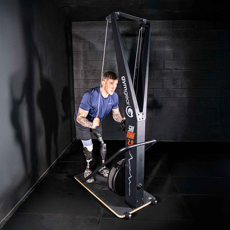 Man using the Gym gear Ski Max 2.0 Ski machine in a dark room with a black wall.