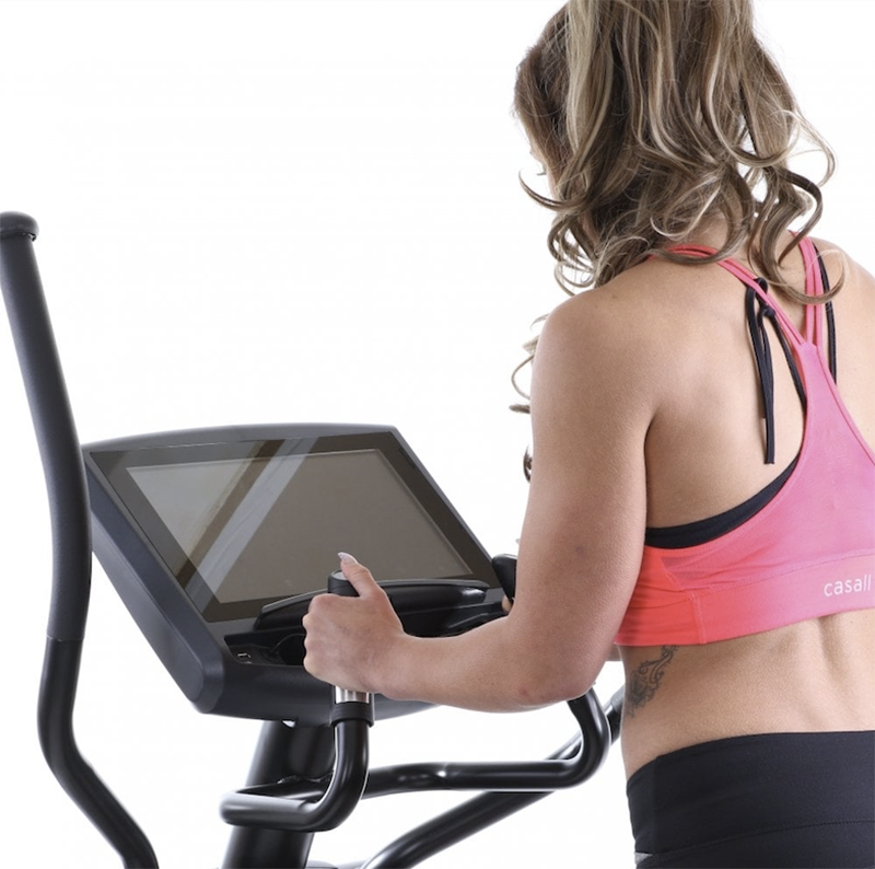 Woman using a Gym Gear X98e Cross Trainer with a screen, wearing a pink sports bra and black leggings.
