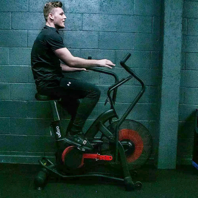 Person using the Origin Storm Air Bike exercise bike against a brick wall