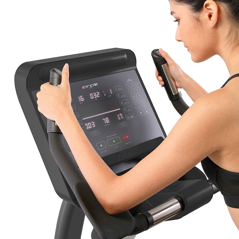 Woman using the Gym Gear C97 Upright exercise bike with a digital display on a white background