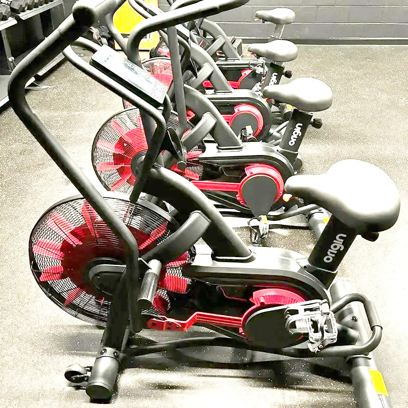 Origin Storm Air Bike exercise bike with red and black design, brand 'origin' visible, on a concrete floor.