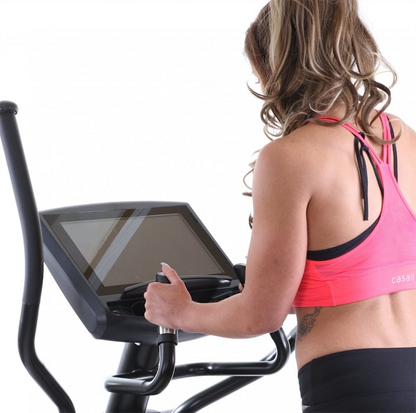 Woman using a Gym Gear X98e Cross Trainer with a screen, wearing a pink sports bra and black leggings.