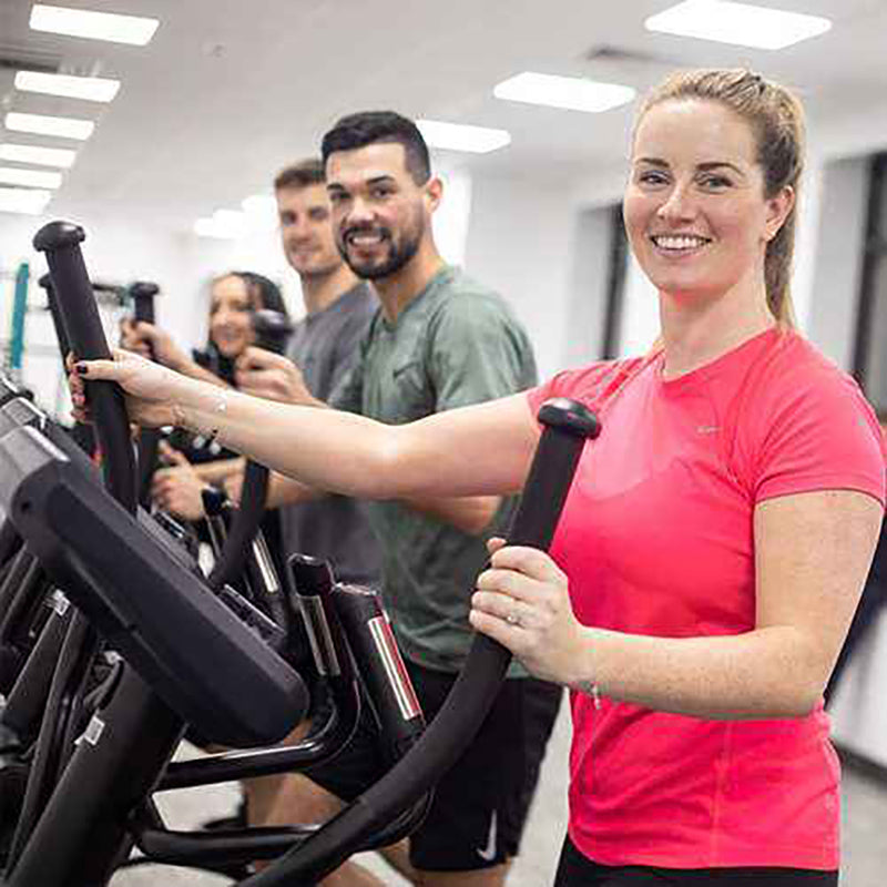Woman exercising on the Gym Gear X97 Cross Trainer elliptical machine with friends in a gym setting