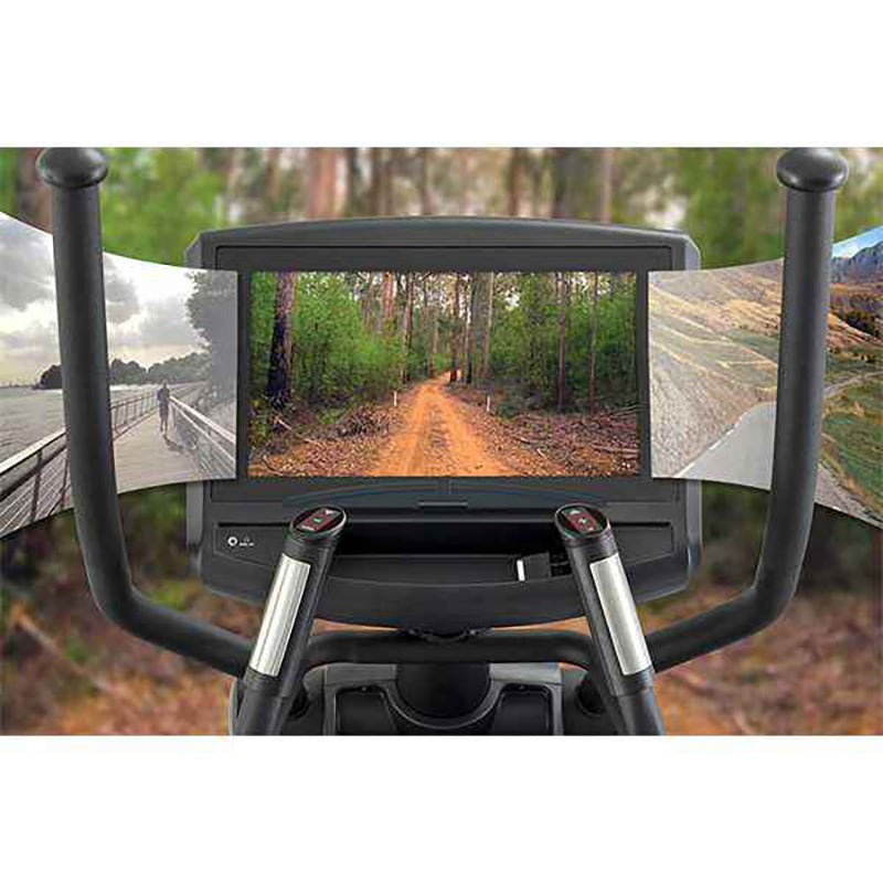 Gym Gear X98e Cross Trainer Ergometer with a screen displaying a forest path, surrounded by nature.